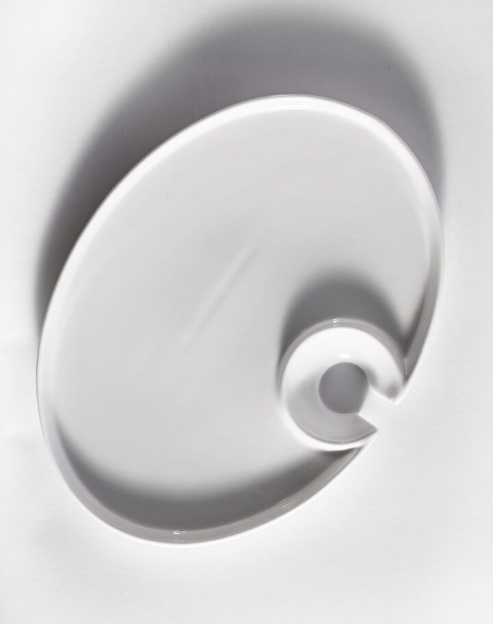 White oval pass plate measuring 10 x 7.5 inches, featuring a unique curved cut-out design for easy handling. Ideal for cocktail service, passed hors d’oeuvres, or modern event presentations.