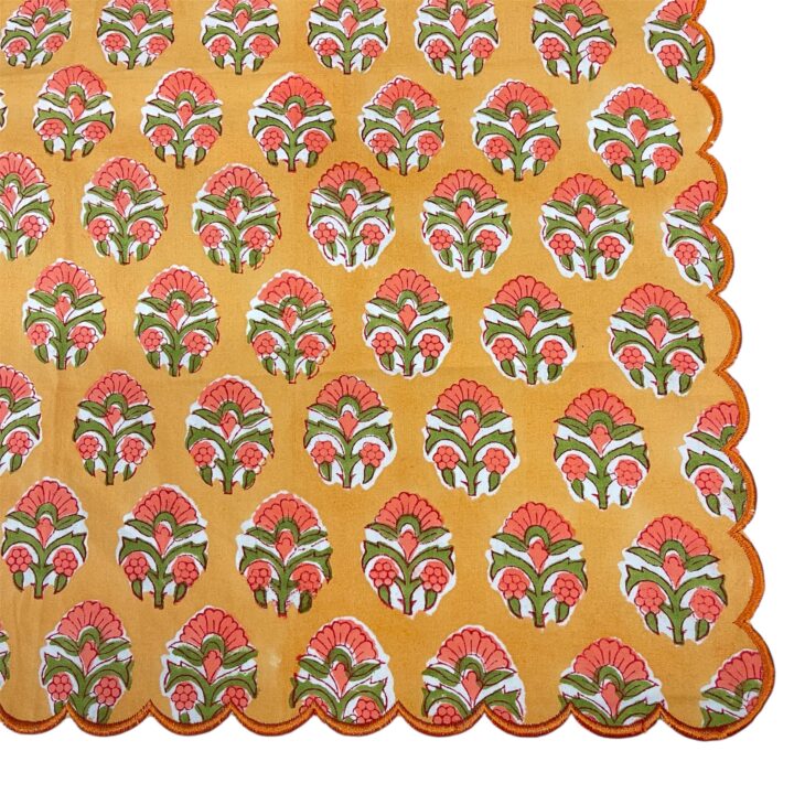 Scalloped dinner napkin in orange and green with a hand-block floral pattern and decorative scalloped edge.