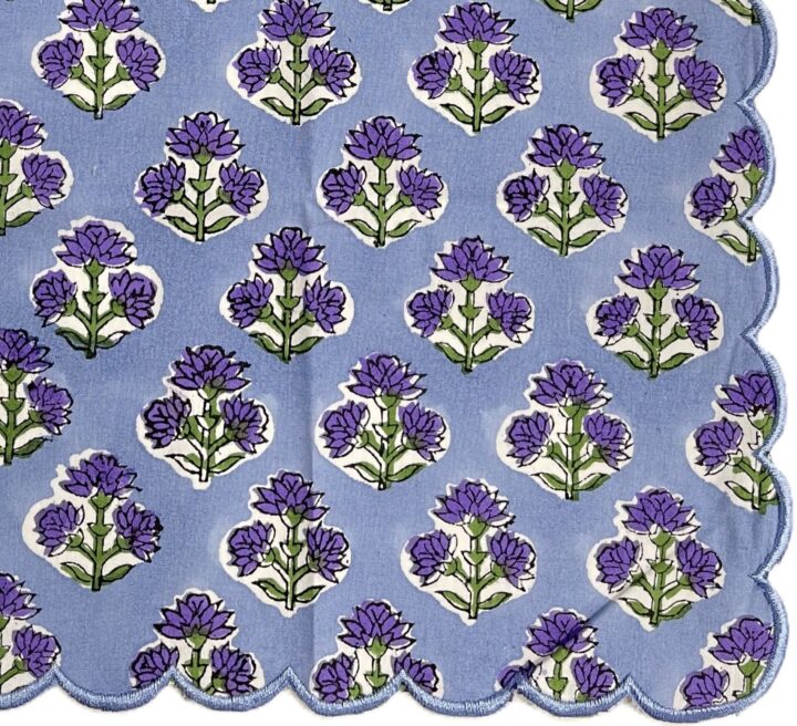 Scalloped dinner napkin in purple and green with a repeating floral design and coordinating scalloped trim.