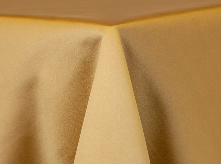 Matte gold satin linen with a smooth, soft sheen draped over a round table, shown in a warm champagne-gold tone.