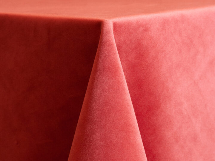 Coral velvet linen with a soft, plush texture draped over a round table, shown in a warm pink-coral hue.