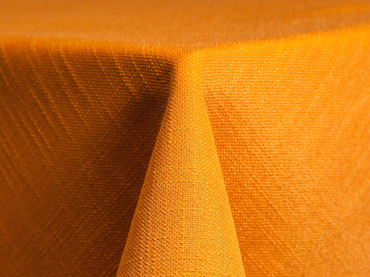 Tangerine Panama linen round tablecloth with soft woven texture, styled on a round event table.