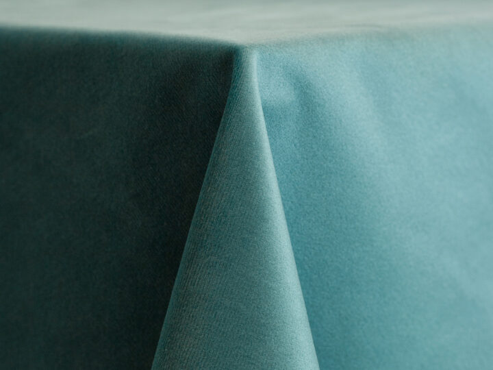 ich ocean blue velvet linen draped over a round table, featuring a soft plush texture with elegant folds and a deep teal tone.